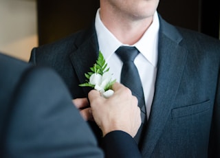 man attaching flower on another man's lapel in a well-lit room