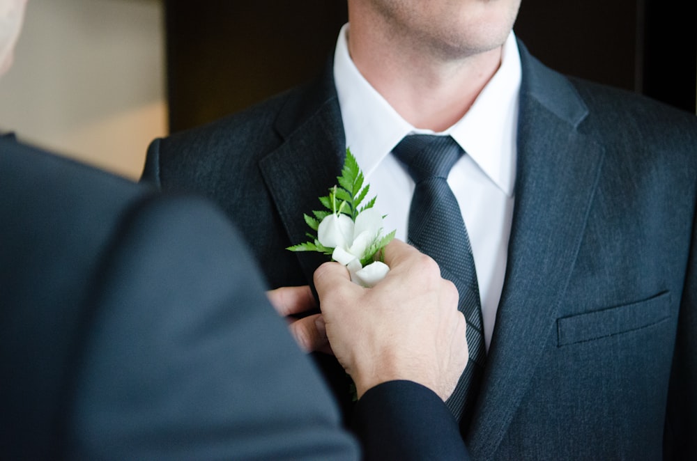 man attaching flower on another man's lapel in a well-lit room