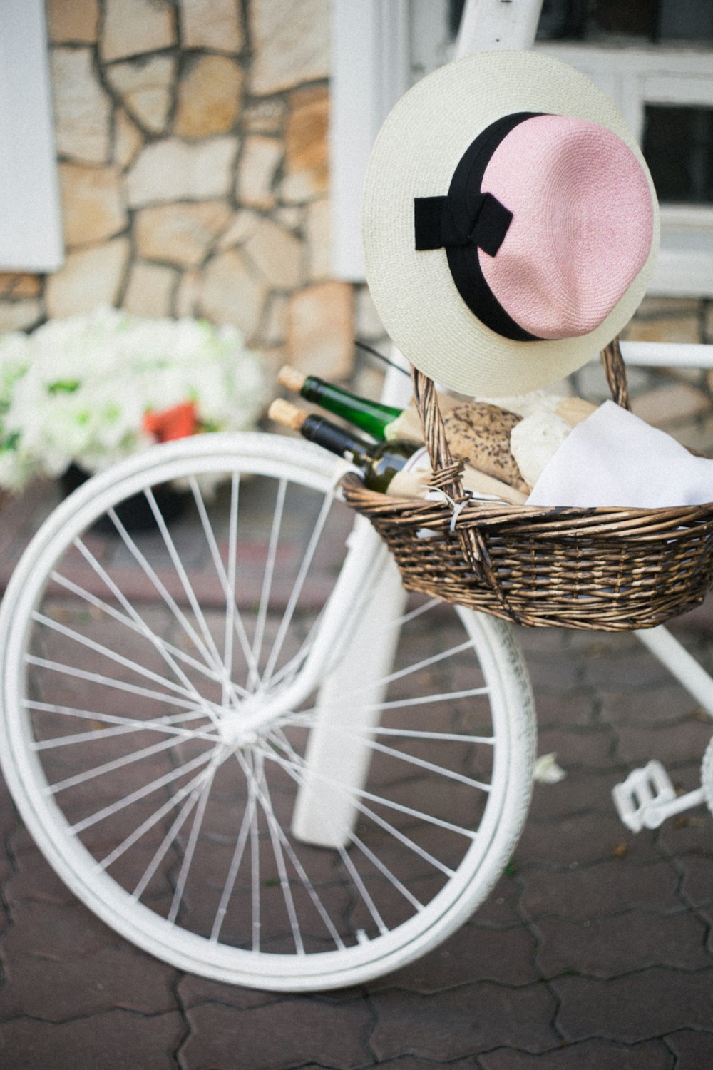 Cesta de mimbre marrón con sombrero para el sol blanco, rosa y negro además de bicicleta blanca