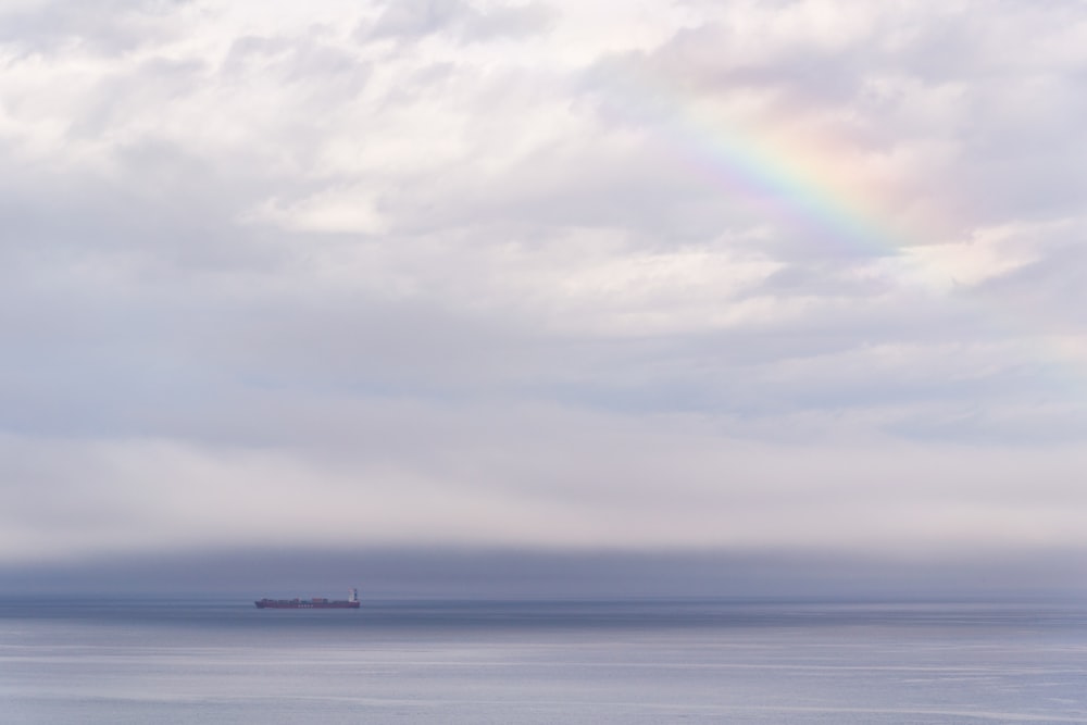 vessel on ocean under cloudy sky with rainbow