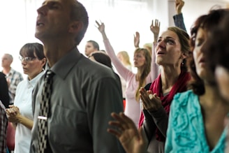 A diverse group of people in prayer circle, eyes closed and hands joined.