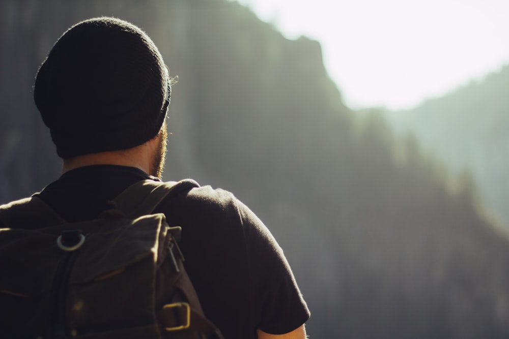 homme portant un t-shirt noir et une casquette en tricot devant des montagnes