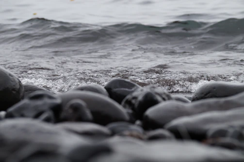 Close-up of gentle waves lapping against smooth stones on a riverbank.