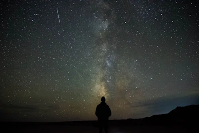 A silhouette of a person standing under a starry sky with colorful auroras.