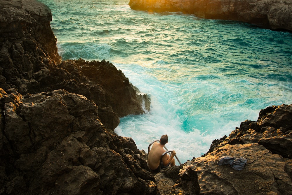 Hombre sentado en una formación rocosa al lado del cuerpo de agua