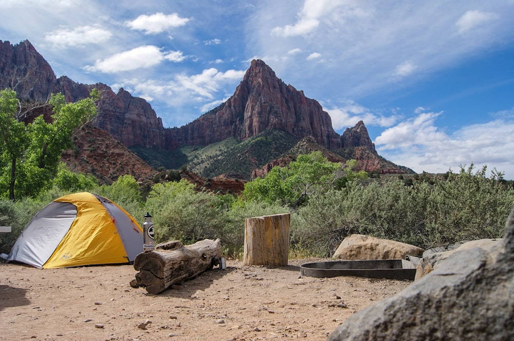 yellow and gray dome tent near tree stump with rocky mountain under cloudy sky