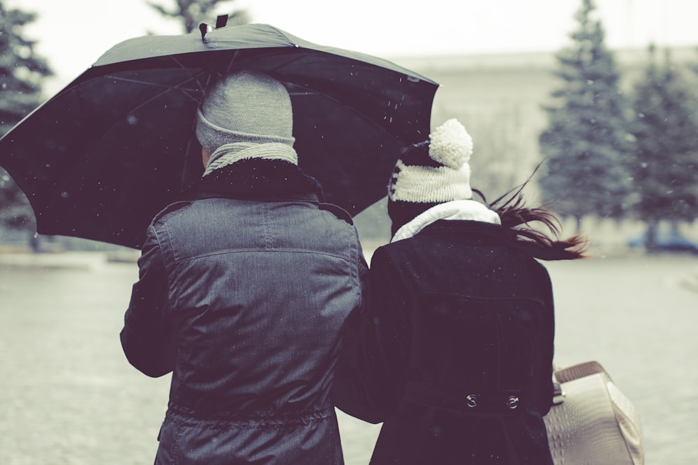 Rückansicht Fotografie von zwei Personen unter Regenschirm an einem verschneiten Tag