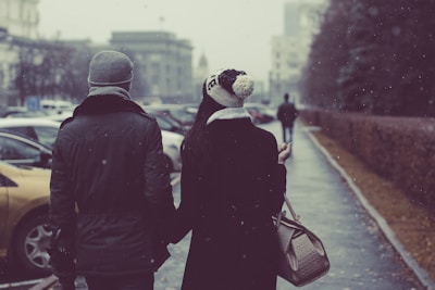 A man and woman walking hand-in-hand wearing matching Thunder Financial winter gloves in a snowy park.