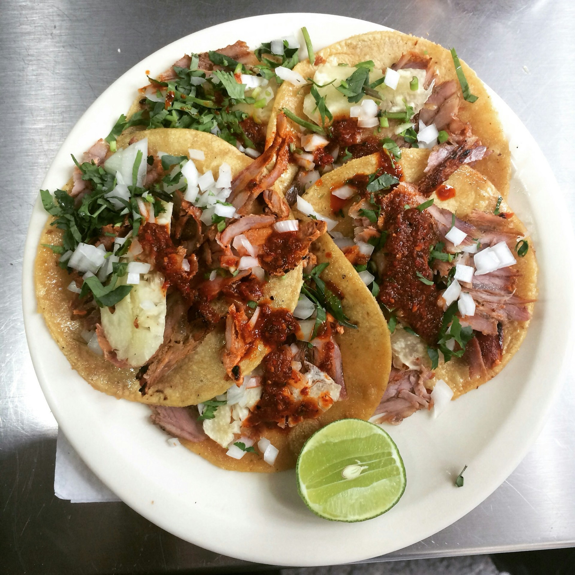 A vibrant plate of colorful tacos topped with fresh ingredients and served with lime wedges.