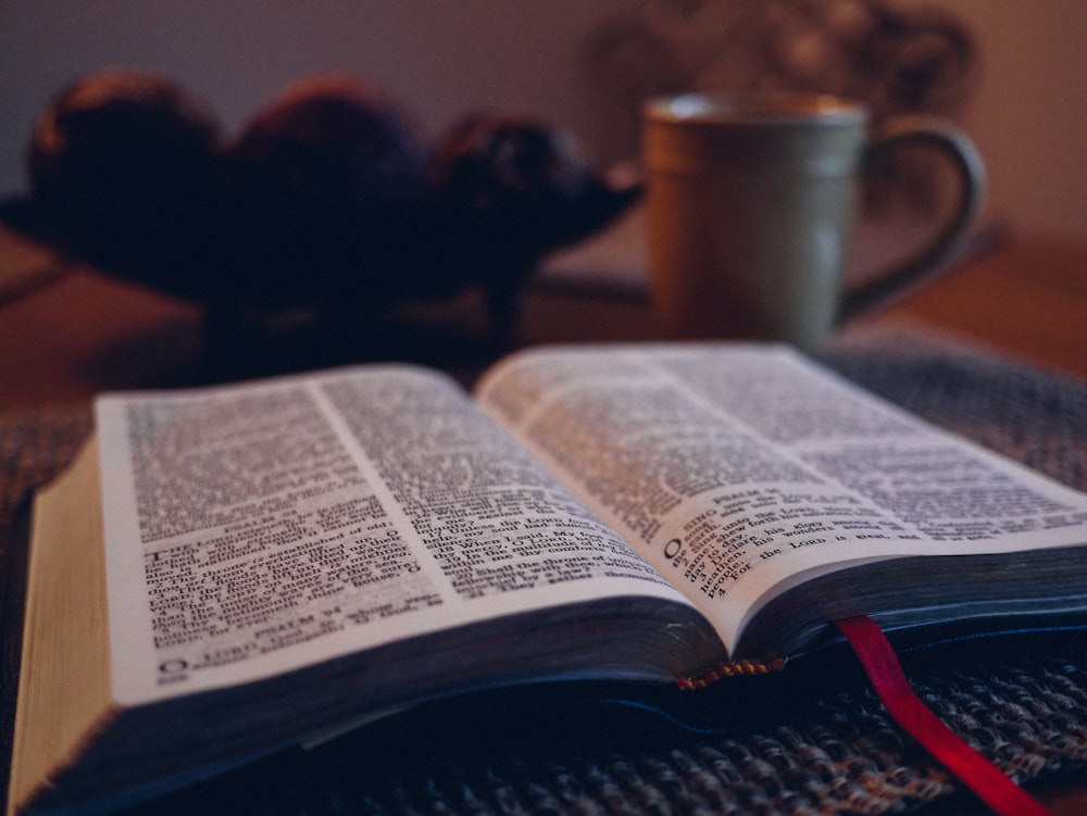 Livre ouvert sur tapis noir à côté d’une tasse en céramique grise