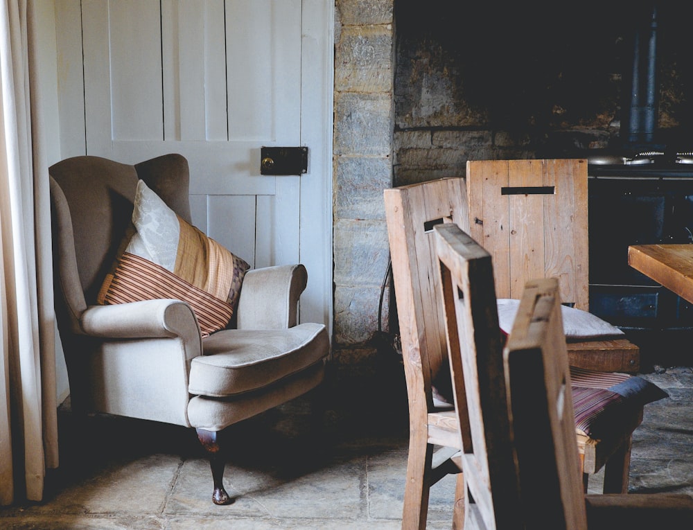 gray wing chair with throw pillows beside white door