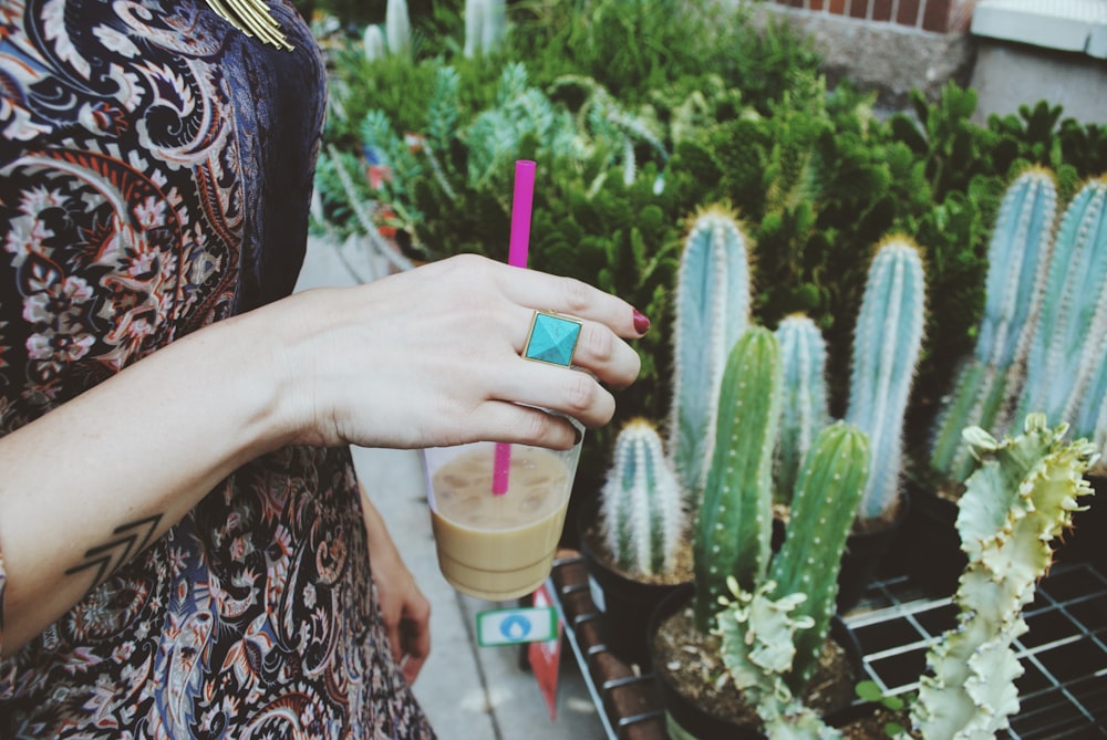 person holding disposable cup in front of cactus plants