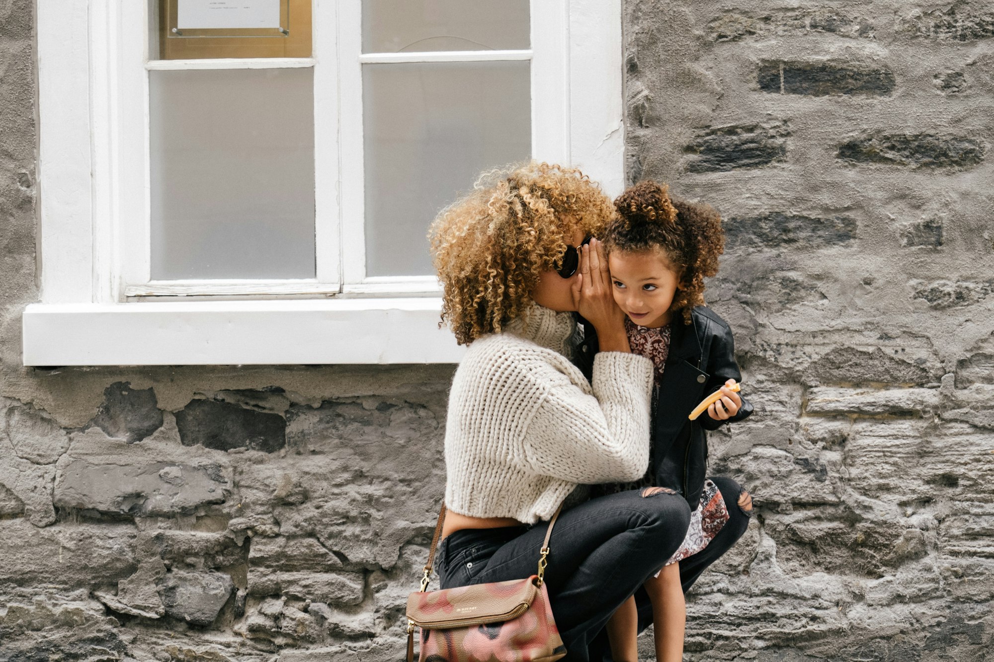A light-skinned black woman crouched down beside her daughter whispering in her ear.