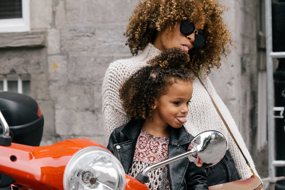 Frau und Mädchen zeigen ihre Zunge neben Motorrad