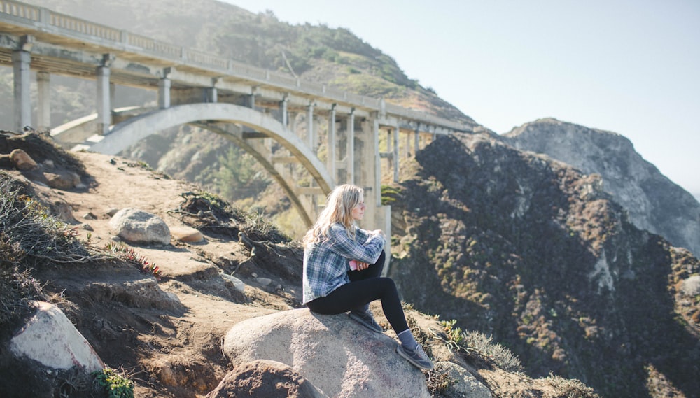 woman wearing plaid shirt sitting on rock