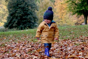 boy wearing orange bubble jacket walking on dry fallen leaves on ground