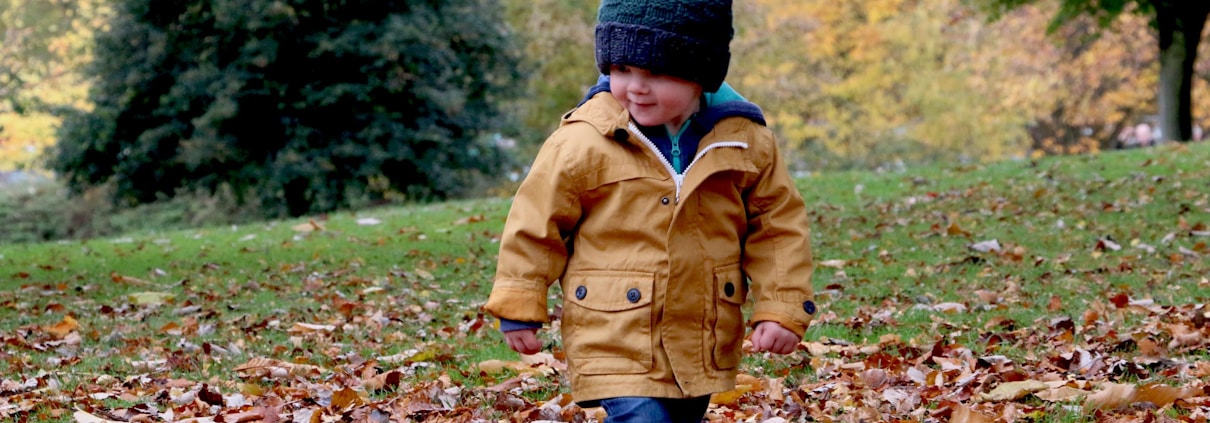 boy wearing orange bubble jacket walking on dry fallen leaves on ground