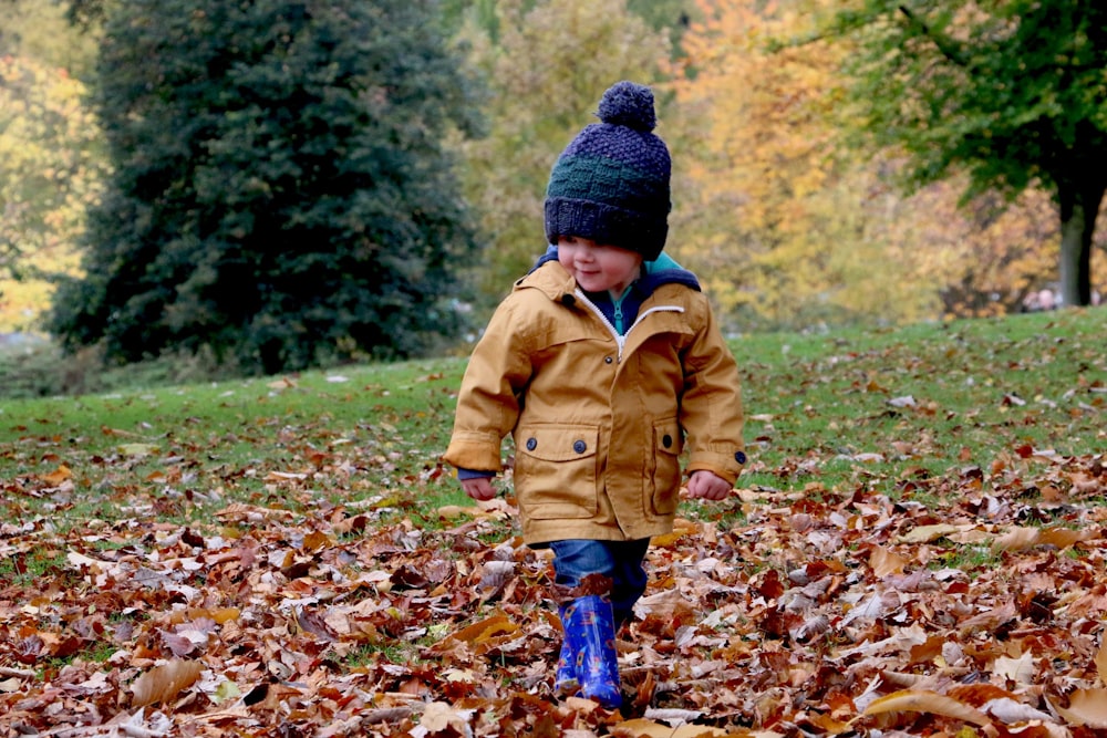 boy wearing orange bubble jacket walking on dry fallen leaves on ground