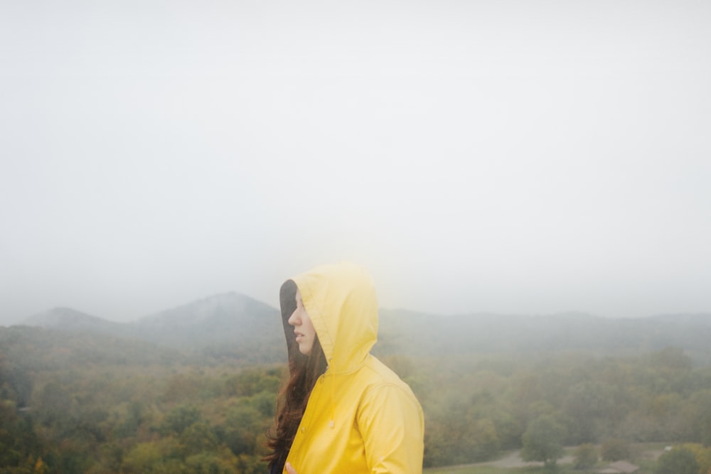 a woman in a yellow raincoat standing on a hill