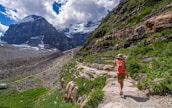 A scenic view of a mountain trail with a person hiking and carrying a backpack.