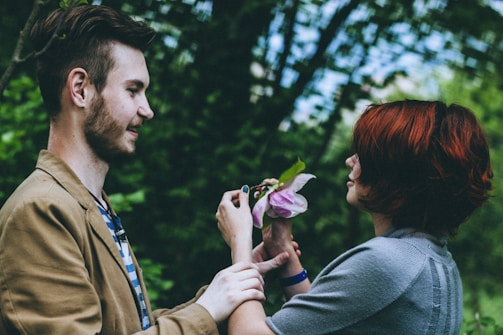 A friendly gardener handing a blooming flower to a smiling customer in a lush green garden.