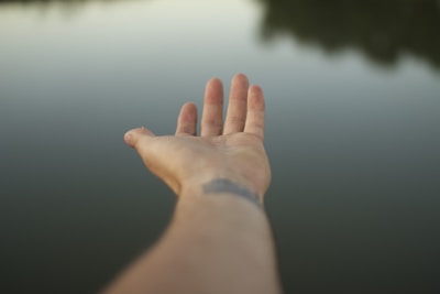 A hand reaching out towards calm, reflective water. The image focuses on the extended arm and hand, inviting a sense of exploration or interaction with nature.