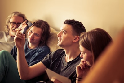 A group of four people sitting together on a couch, attentively looking at photographs. The mood seems relaxed and nostalgic. Everyone appears to be engaged with the photos, which are being held by one of the individuals.