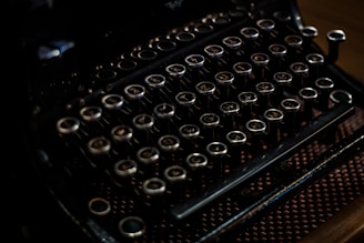 An antique typewriter with round, metallic keys, featuring a dark, vintage aesthetic and intricate detailing.