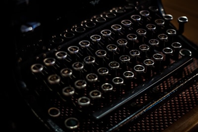 An antique typewriter with round, metallic keys, featuring a dark, vintage aesthetic and intricate detailing.