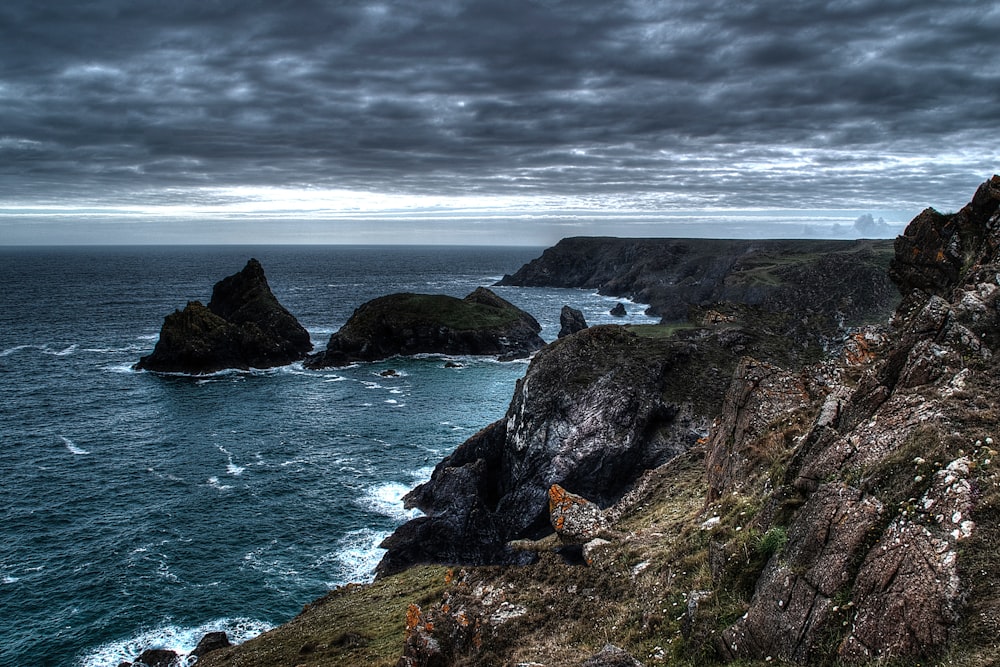 cliff beside body of water during cloudy day