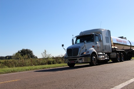 A large cargo truck driving on a highway surrounded by green fields under a clear blue sky.
