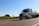 Truck driving on a highway surrounded by green fields under a clear sky.