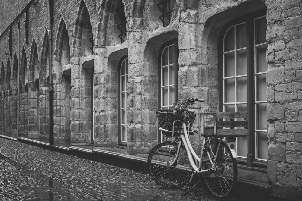 grayscale photo of bike parked beside building