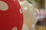 Several balloons, predominantly red with white polka dots, are lined up in a blurred background. The focus is on a single red balloon with white polka dots, creating a playful and festive atmosphere.