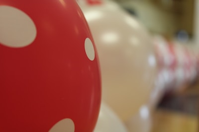 Several balloons, predominantly red with white polka dots, are lined up in a blurred background. The focus is on a single red balloon with white polka dots, creating a playful and festive atmosphere.