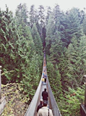 Adventure seekers crossing a wooden suspension bridge surrounded by dense greenery.
