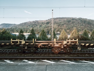 Rail freight cars loaded with large industrial parts moving through a scenic countryside.