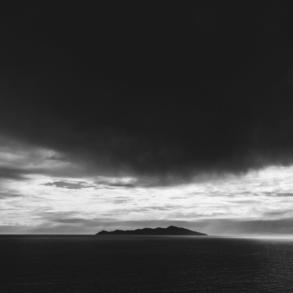 greyscale photo of an island under white clouds