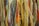 A close-up of various strands of yarn in multiple colors, including shades of yellow, green, red, blue, and brown. The yarn is textured, with some strands appearing thick and others thin, creating a layered and vibrant appearance.