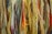 A close-up of various strands of yarn in multiple colors, including shades of yellow, green, red, blue, and brown. The yarn is textured, with some strands appearing thick and others thin, creating a layered and vibrant appearance.