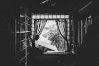 A peaceful scene of Tai journaling beside a window with soft lilac curtains.