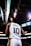 A basketball player wearing a white jersey with the number 10 and the name 'Burks' stands on a basketball court. The arena's ceiling and lights are visible above, along with electronic screens displaying game information.