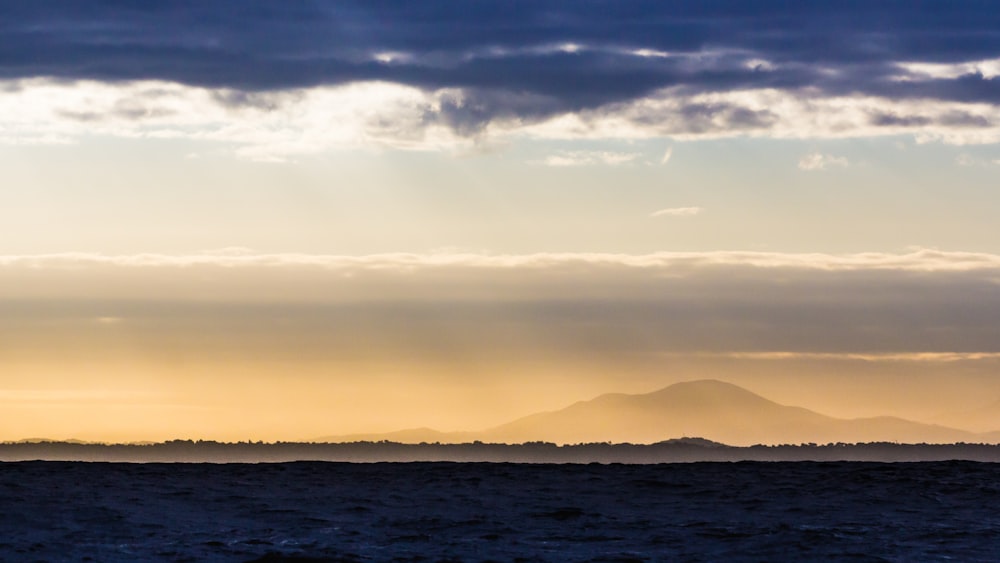 silhouette of road and mountain under gray clouds at golden hour