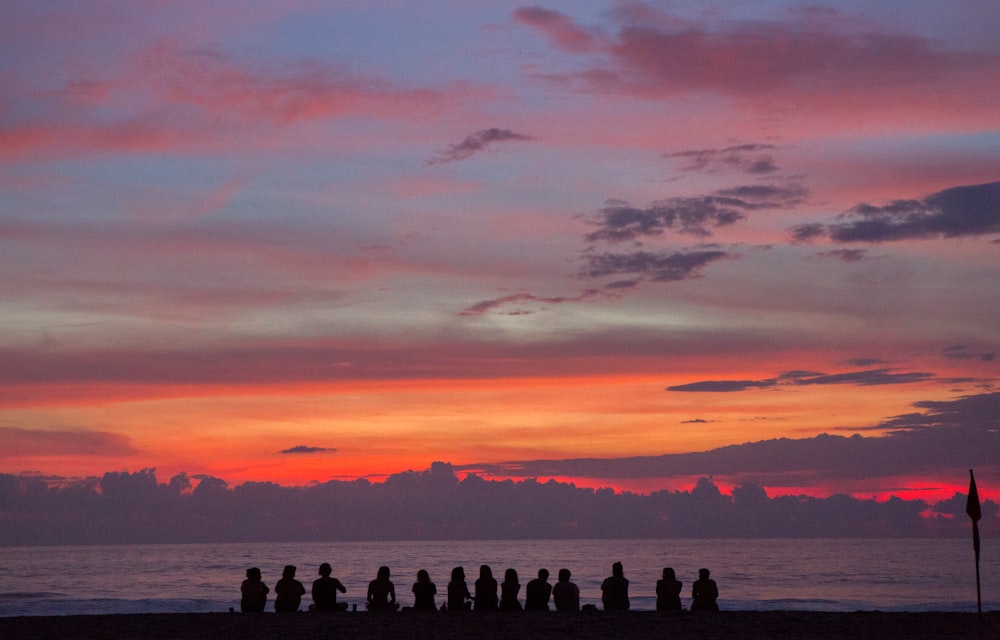 Thirteen people are silhouetted against a setting sun coloring the sky vibrantly
