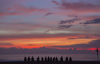 people sitting on seashore while watching golden hour