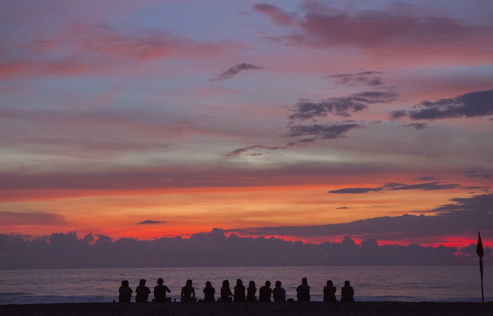 people sitting on seashore while watching golden hour