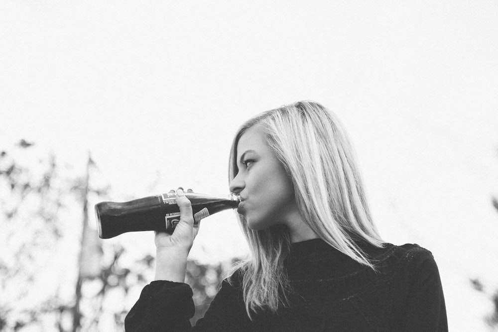 Black and white shot of attractive blonde woman drinking cola from glass bottle