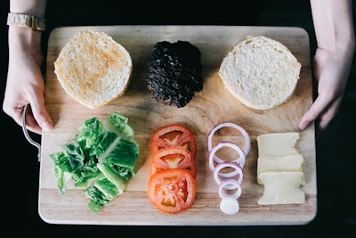 Hands shaping fresh burger patties on a wooden board with spices and ingredients around