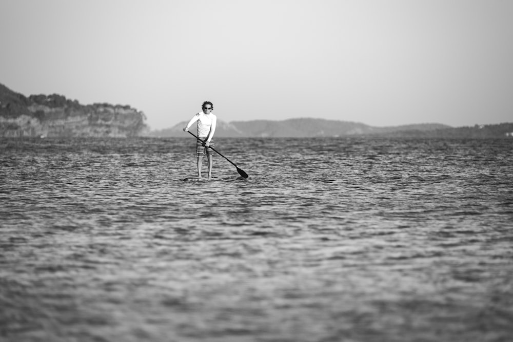 Photo en niveaux de gris d’un homme homme sur une planche de surf pendant la journée