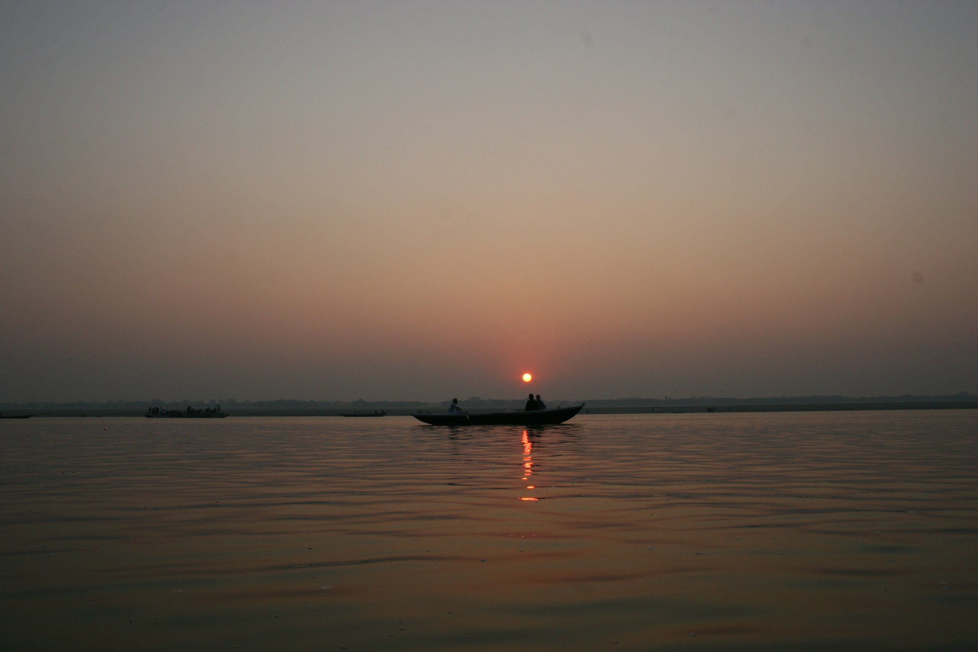 A romantic couple enjoying a private boat ride at sunset on the Bay of Bengal, with hues of golden orange reflecting on calm waters.